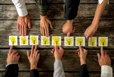 People pointing at cards with 'idea' bulbs representing the sharing of institutional knowledge.