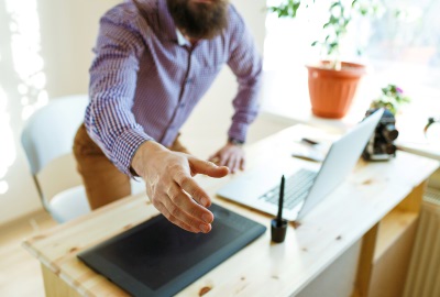 Person reaching out from behind desk offering a handshake depicting the role of the project sponsor and mentor.