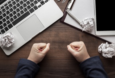 Image of person at computer with clenched fists trying to cope with troubled projects.